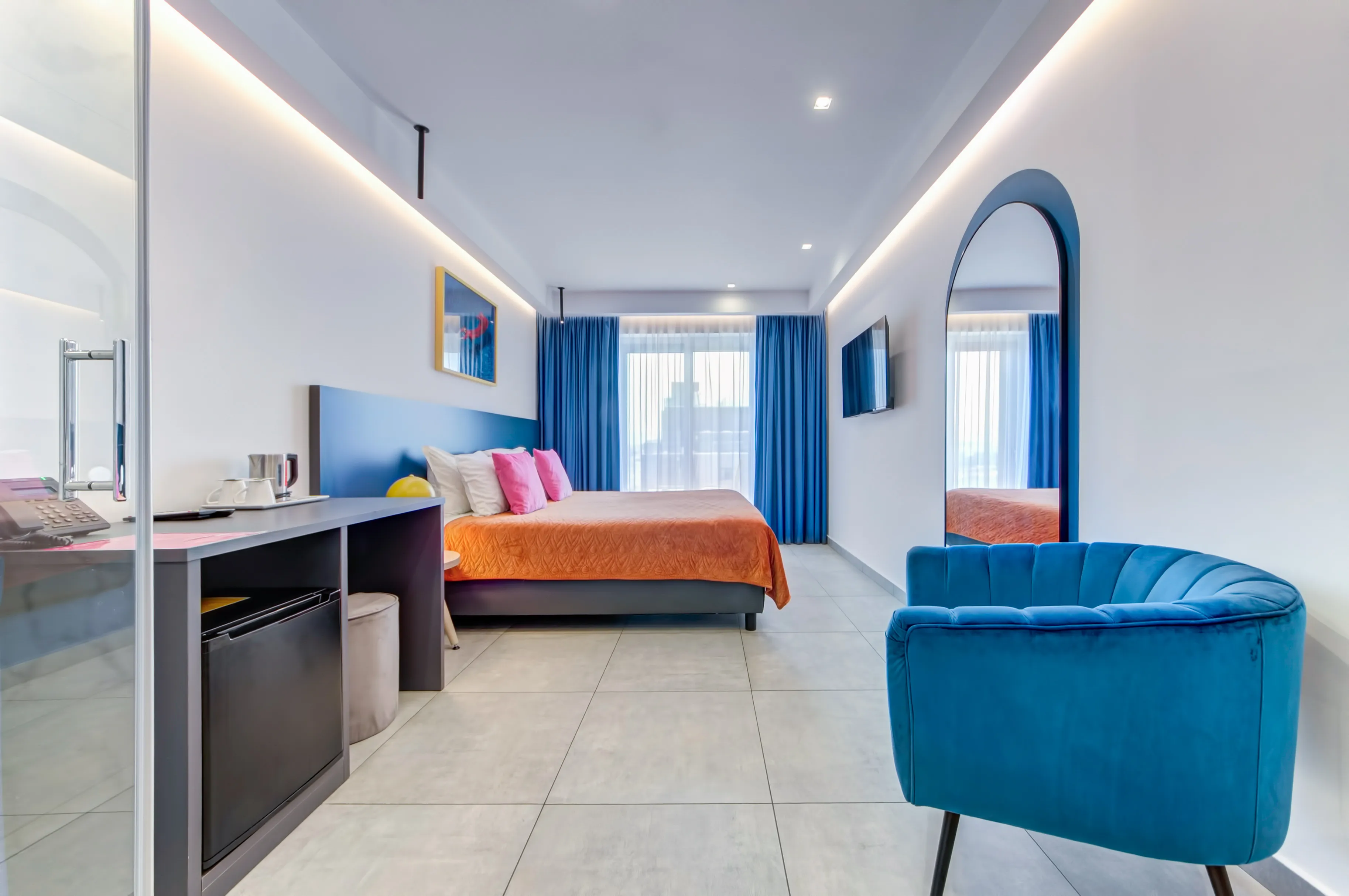 Standard Deluxe Room with blue headboard, orange bedspread, arch mirror and blue velvet chair